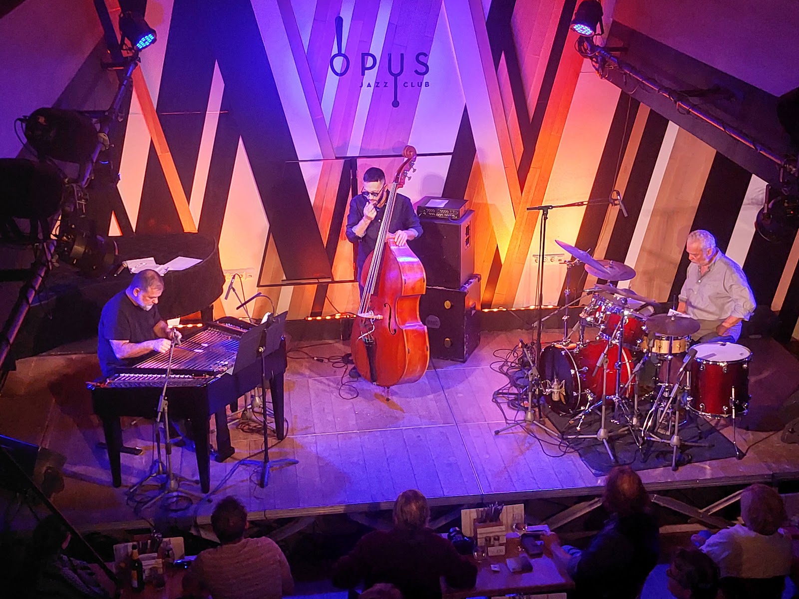 Jazz musicians performing on a small club stage in low light, similar in mood to Opus Jazz Club Budapest