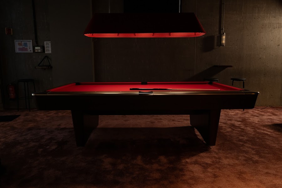 Pool table under hanging lights with a sports screen behind